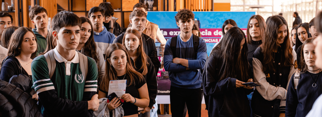 Una treintena de estudiantes de escuelas secundarias, de pie, escuchando atentamente dentro del hall central de la Facultad lo que dice la guía de un Eco Tour, en un día soleado